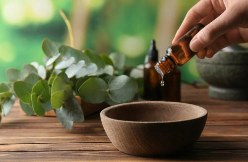 Hand pouring natural botanical oil into a wooden bowl, illustrating the careful sourcing of premium ingredients.