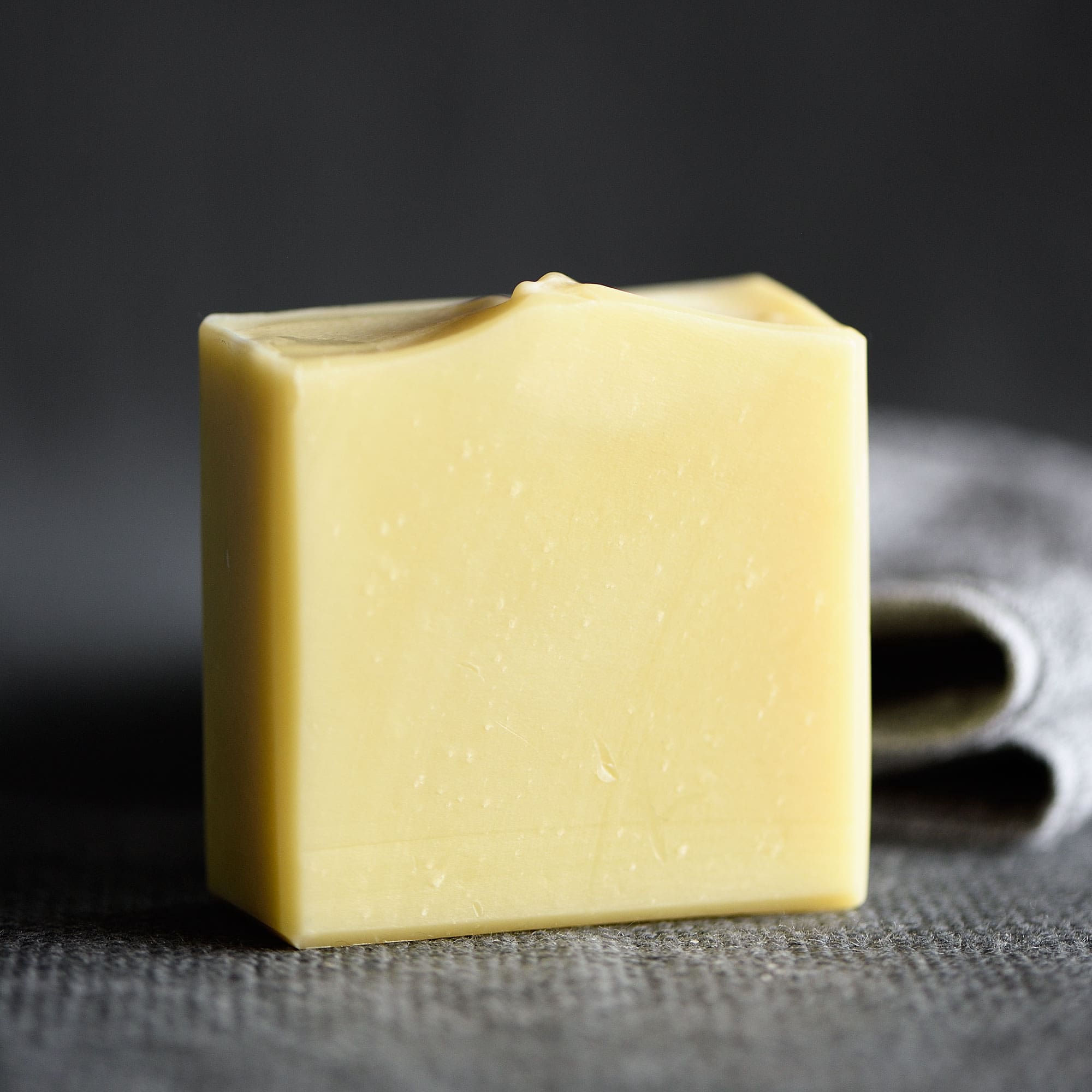Handcrafted unscented body soap bar, pale cream, resting on grey cloth