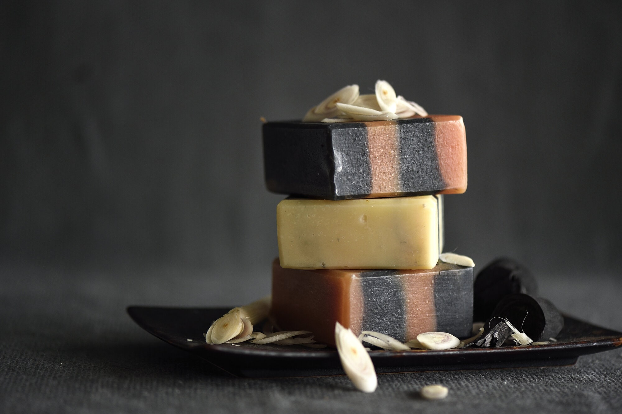 Stack of three handcrafted body soaps in different colours surrounded by lemongrass and charcoal