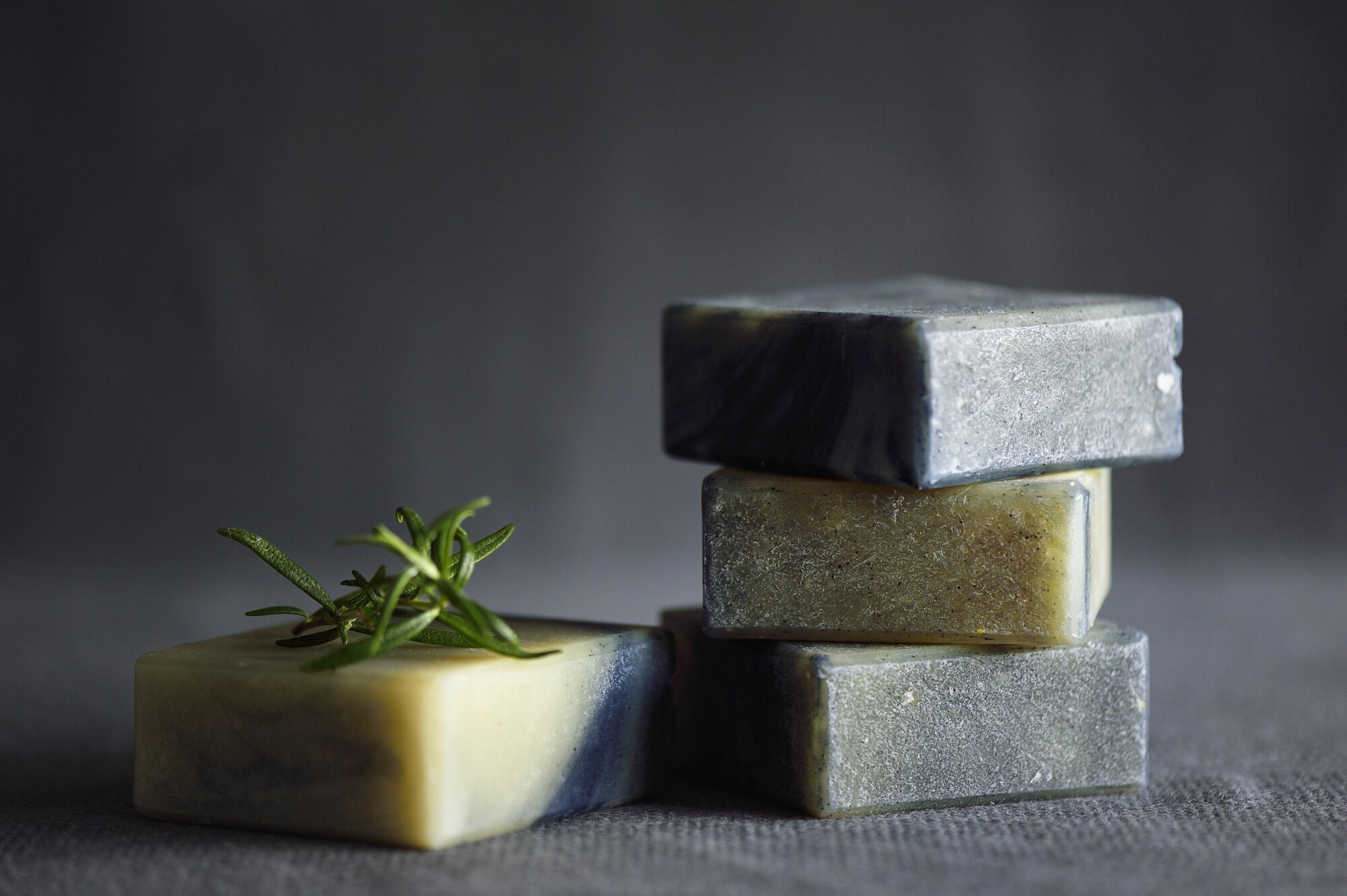 Stack of three gentle face soaps in natural tones displayed with fresh rosemary